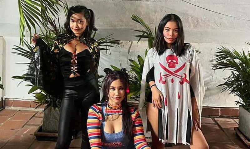 Hình ảnh một người lớn (có thể là cha mẹ) đi cùng hai đứa trẻ mặc trang phục Halloween đang vui vẻ trên vỉa hè trong khu phố được trang trí đèn sáng, nhấn mạnh tầm quan trọng của an toàn cho trẻ em vào đêm Halloween là ngày mấy.