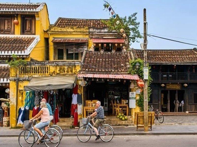 Một chiếc taxi di chuyển trên con đường ngoại ô Tam Kỳ hướng về Hội An, khung cảnh có cánh đồng lúa xanh mướt và hàng cây, thể hiện lộ trình di chuyển giữa hai địa điểm du lịch này.